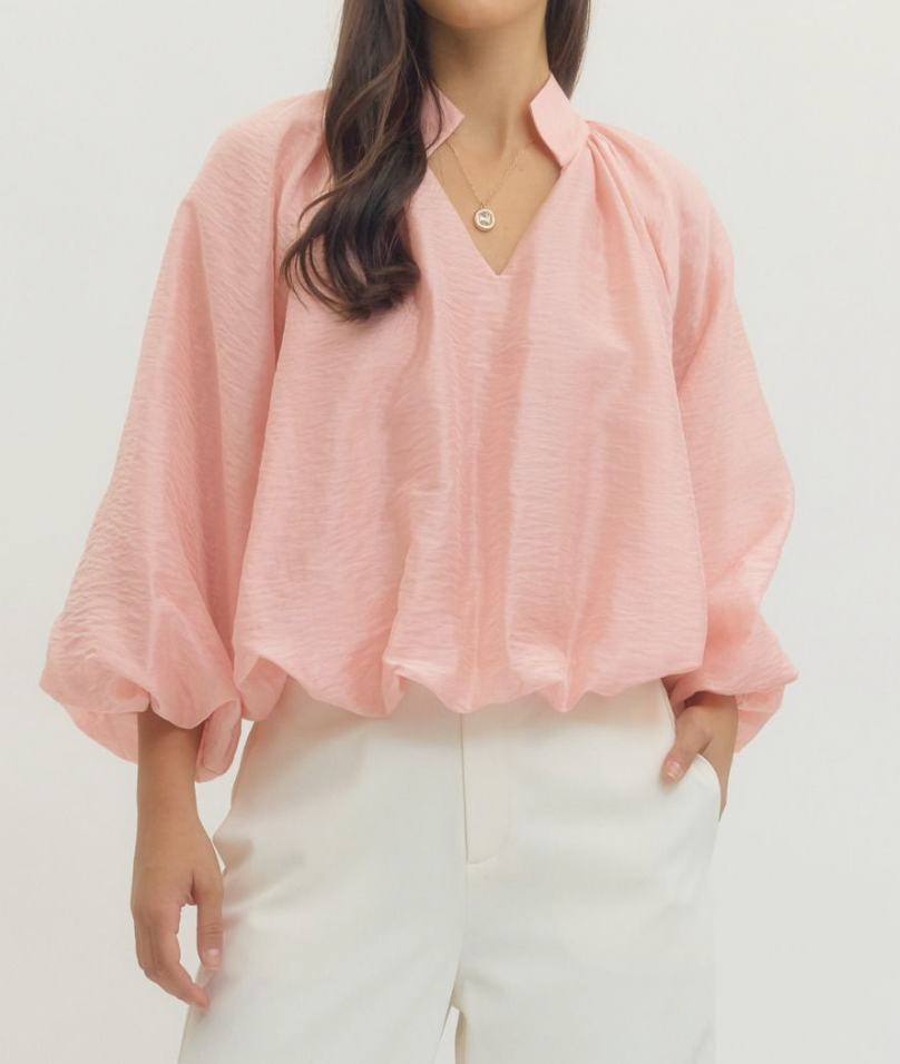 Person wearing a light pink blouse with a plain background