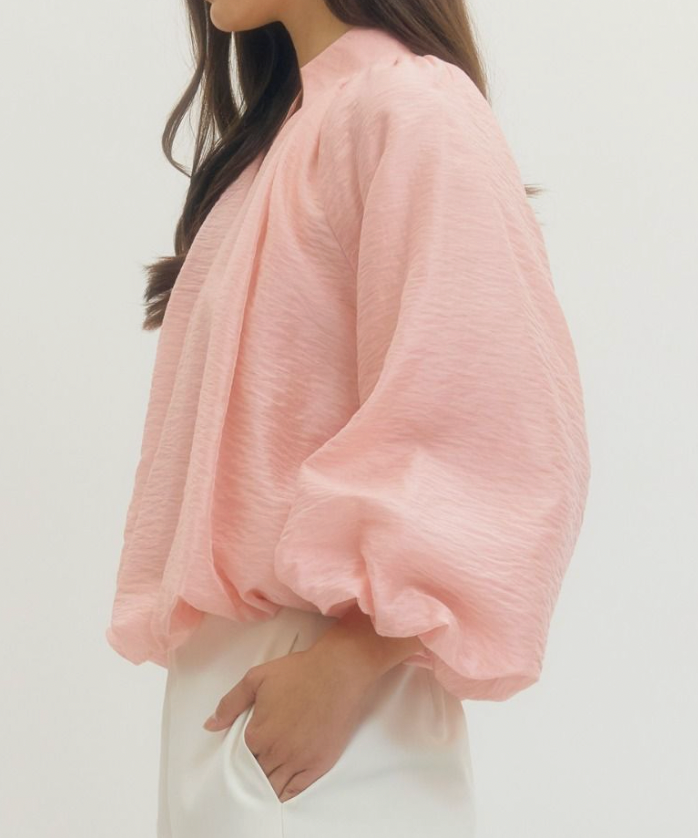 Person wearing a light pink blouse with puffed sleeves on a plain background
