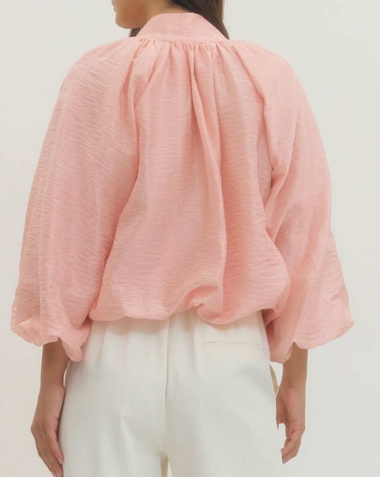 Person wearing a light pink blouse and white pants on a plain background