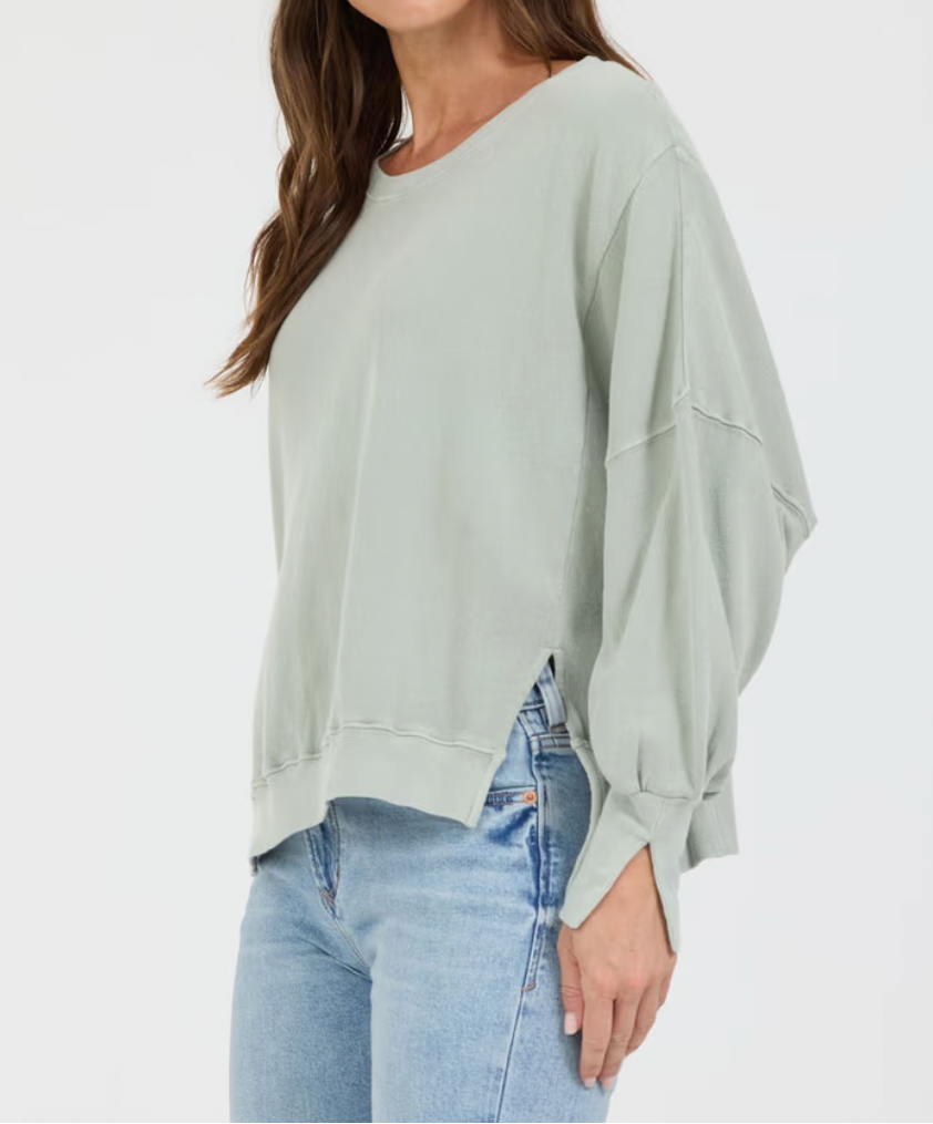 Woman wearing a light green oversized sweater and blue jeans on a white background