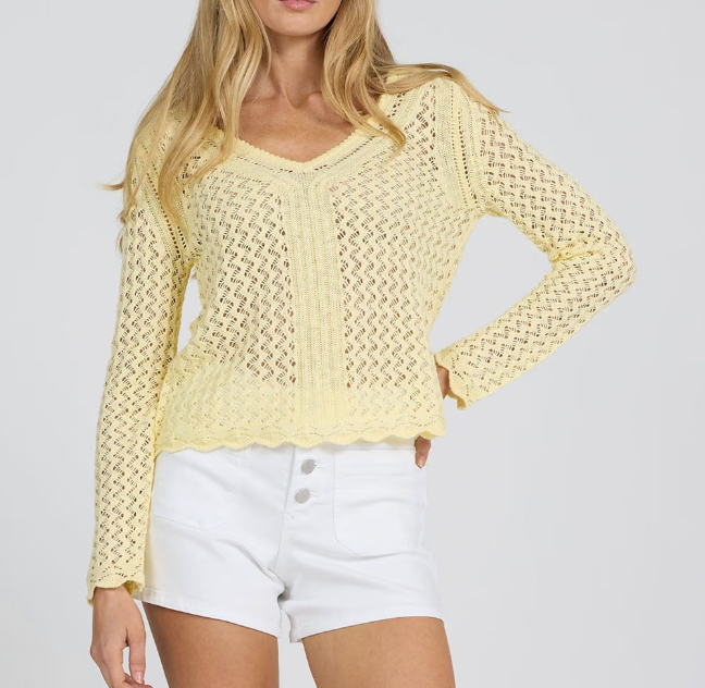 Woman wearing a light yellow crochet top and white shorts on a plain background