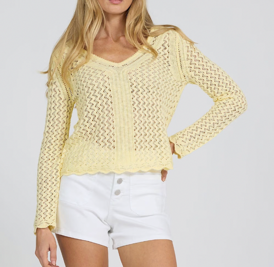 Woman wearing a light yellow crochet top and white shorts on a plain background