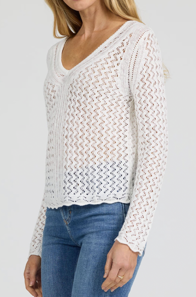 Woman wearing a white lace long-sleeve top and blue jeans on a plain background