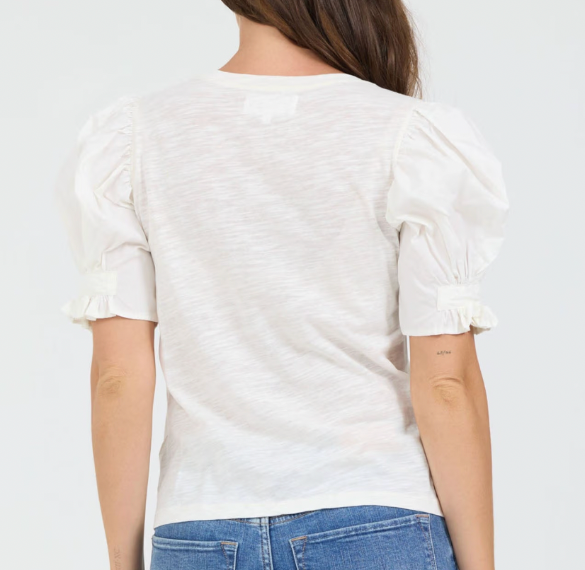 Person wearing a white blouse with puff sleeves and blue jeans on a plain background