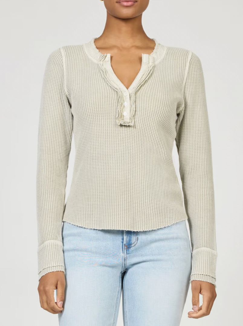 Woman wearing a beige ribbed long-sleeve top with a V-neck and light blue jeans on a white background