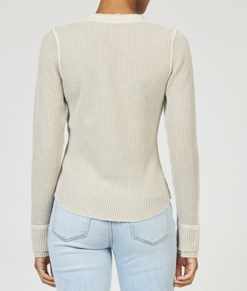 Person wearing a beige ribbed sweater and light blue jeans on a plain background