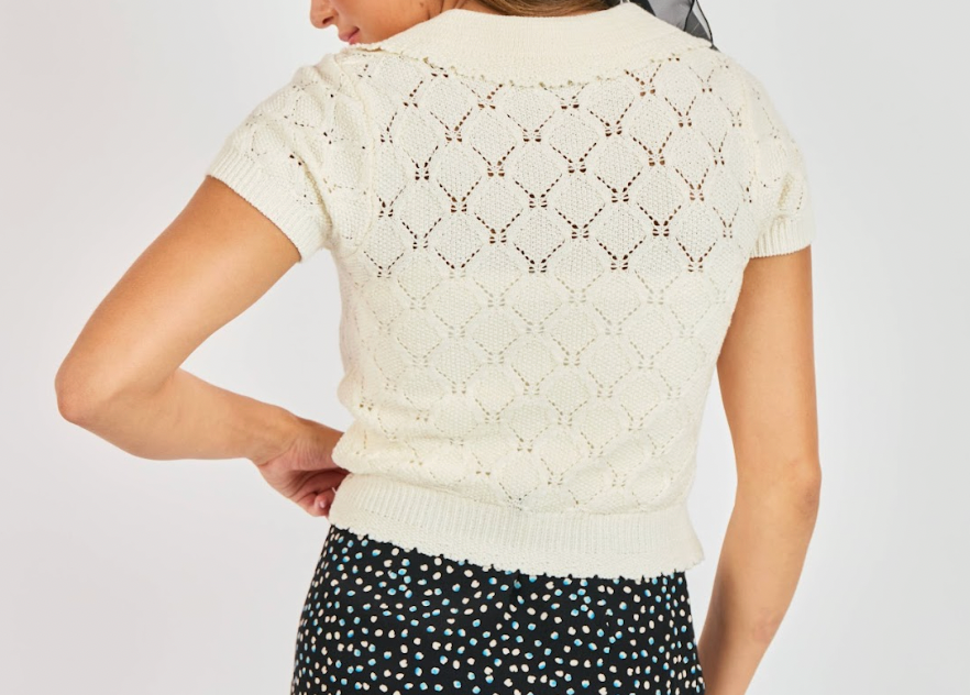 Person wearing a white lace top with a plain background