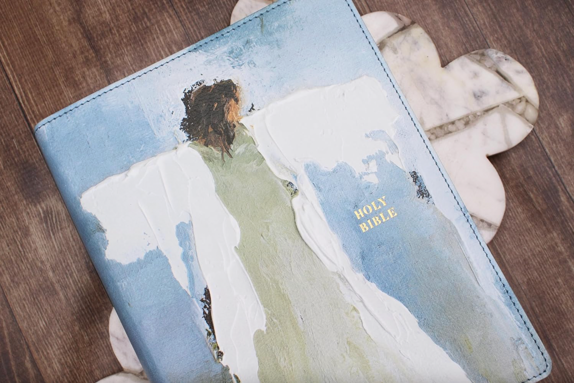 Bible cover with artistic design of a woman on a mountain, placed on a wooden surface.