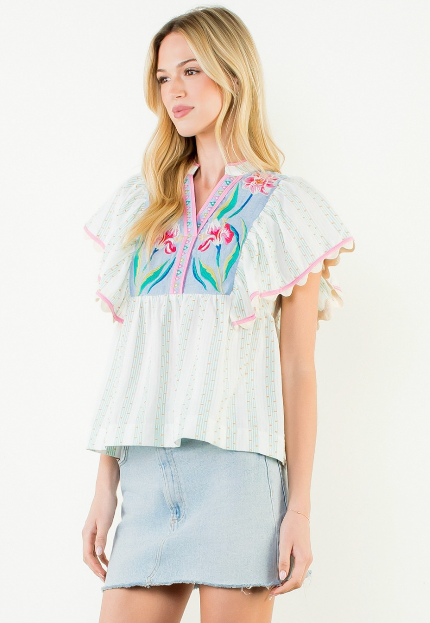 Woman wearing a colorful embroidered blouse with a denim skirt on a white background