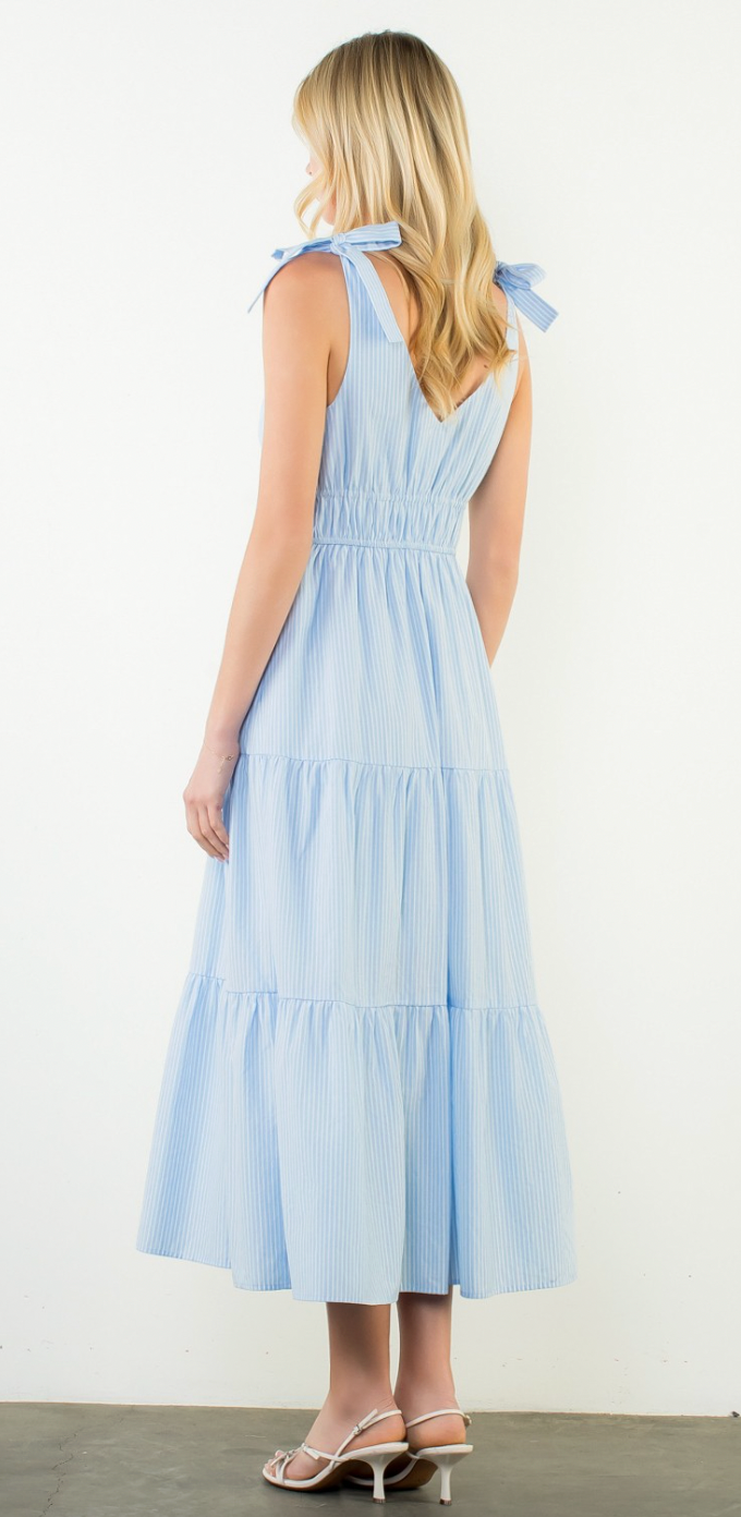 Woman wearing a light blue dress with tiered skirt and bow straps on a white background