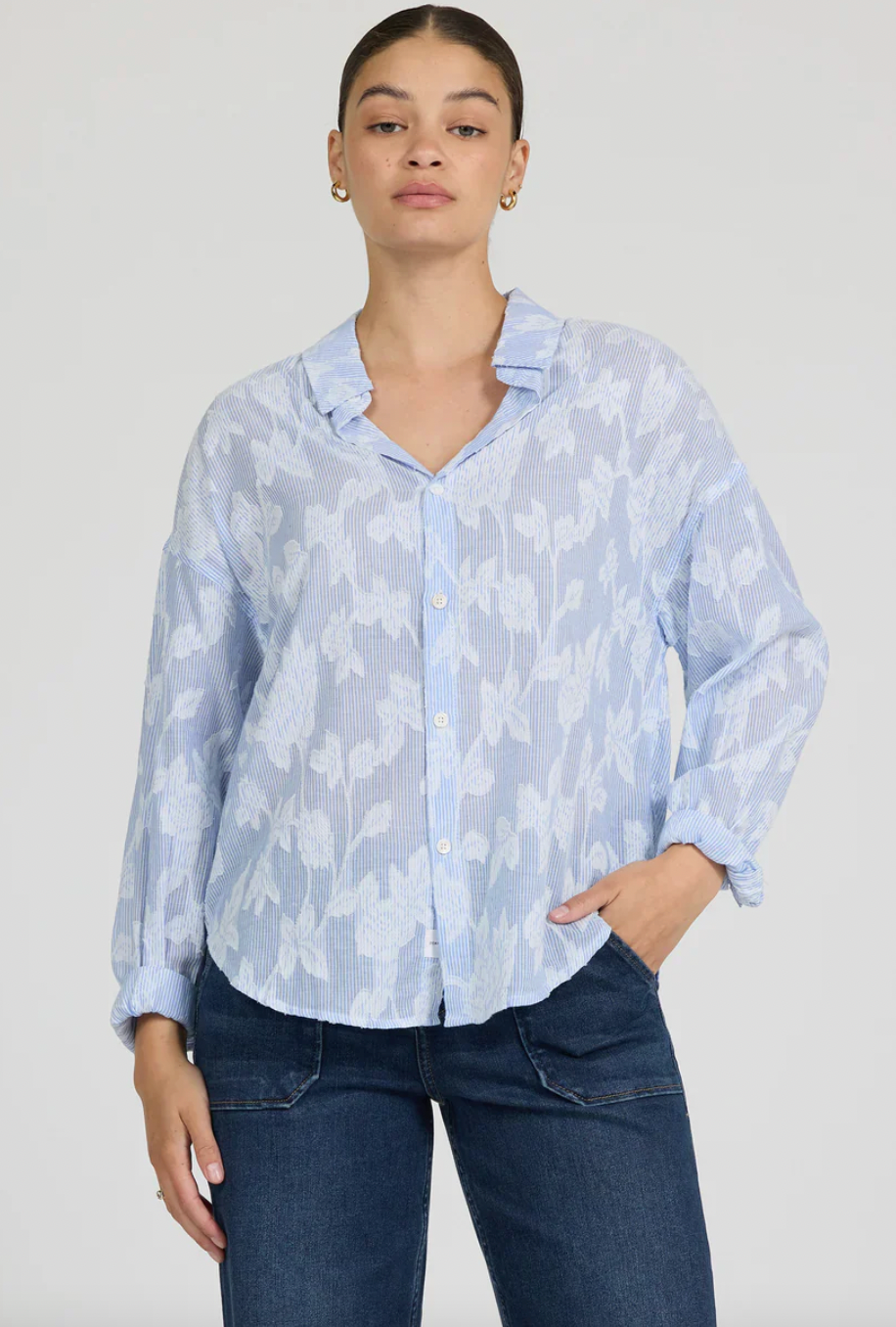 Woman wearing a light blue floral blouse and dark jeans on a white background