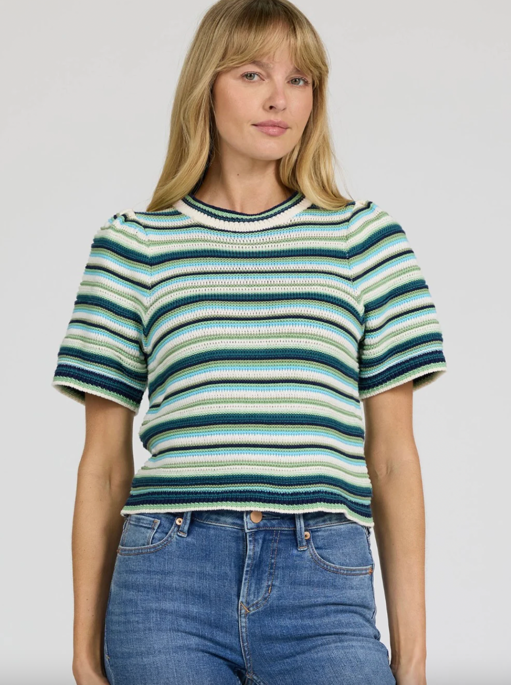 Woman wearing a striped shirt and jeans on a plain background
