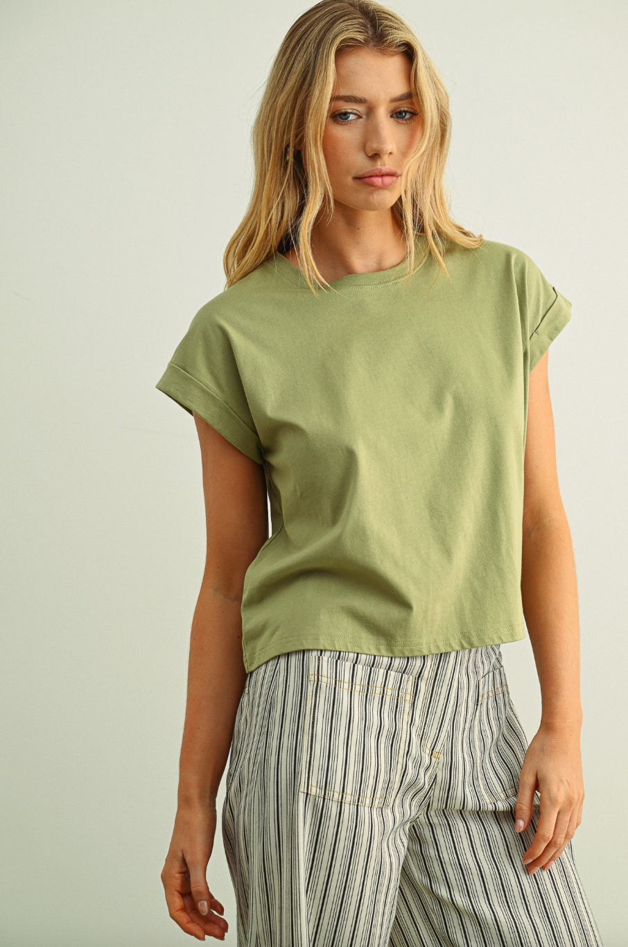 Woman wearing a green t-shirt and striped pants against a plain background