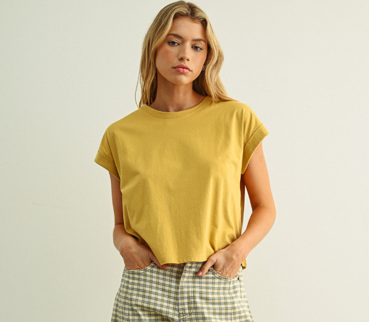Woman wearing a yellow t-shirt and plaid shorts against a plain background