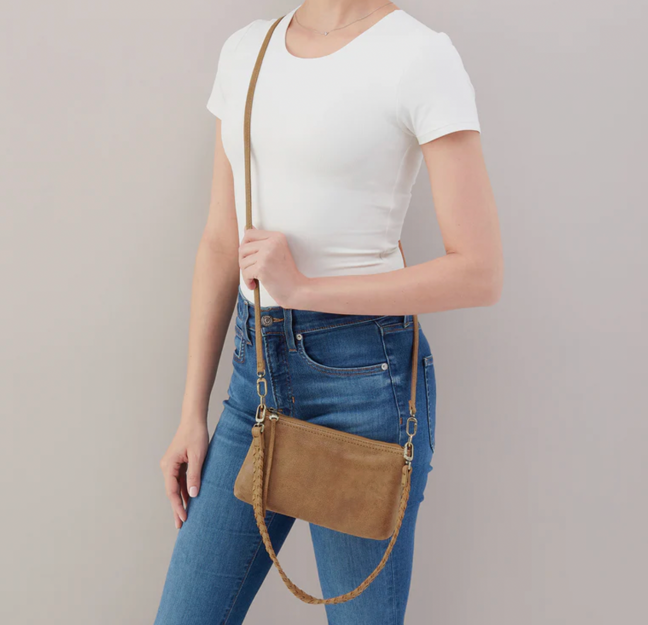 Person wearing a white t-shirt and blue jeans with a brown leather crossbody bag on a plain background