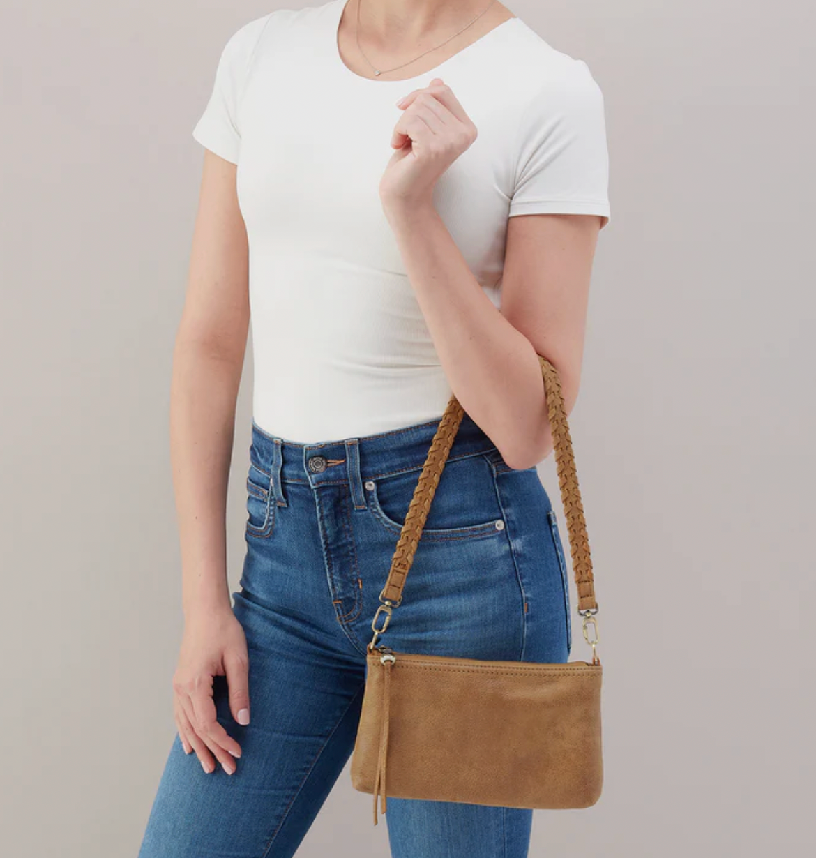 Person wearing a white t-shirt and blue jeans with a brown leather bag on a plain background
