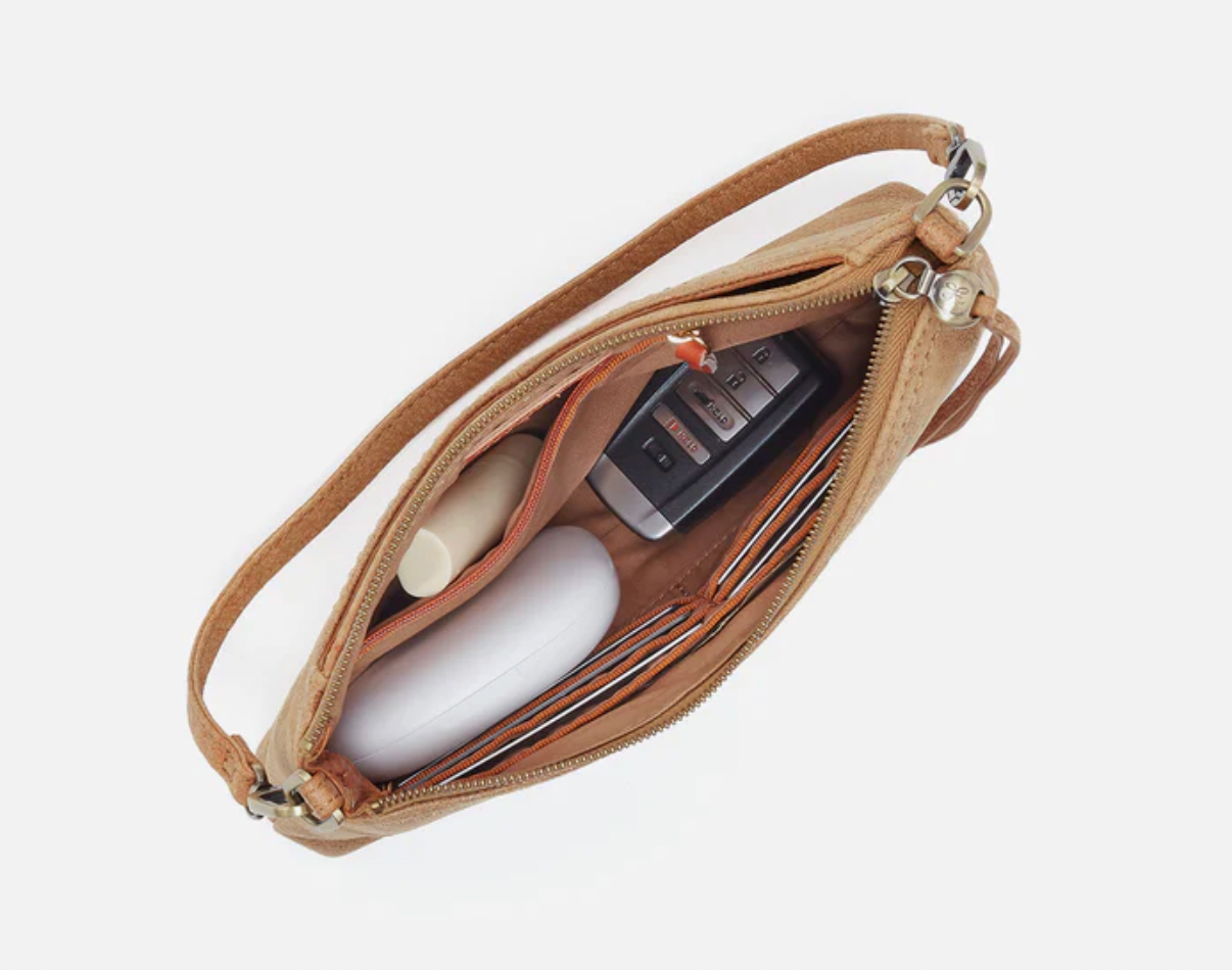 Beige crossbody bag with phone and white item on a light gray background