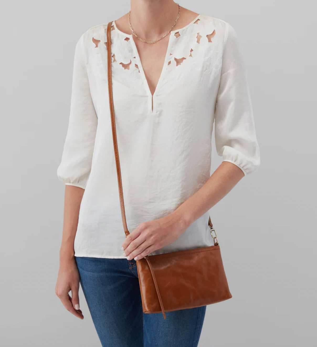 Person wearing a white blouse with bird patterns and holding a brown leather bag on a gray background