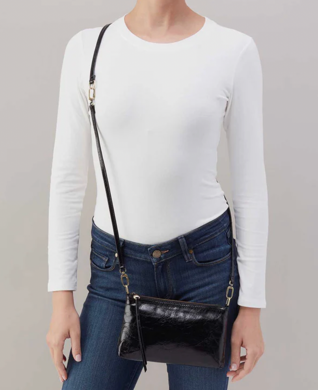 Person wearing a white long-sleeve top and blue jeans with a black handbag on a gray background