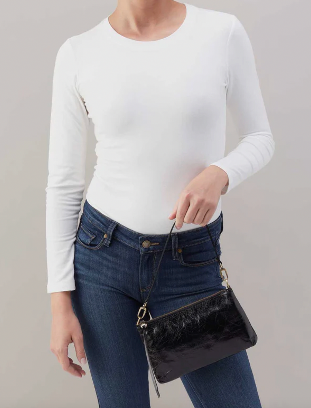 Person wearing a white long-sleeve top and blue jeans, holding a black handbag against a plain background