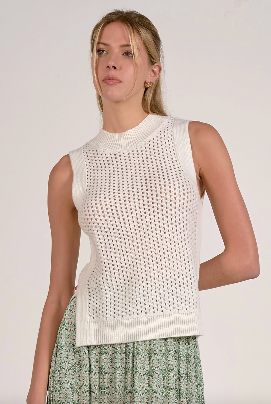 Woman wearing a sleeveless white knit top against a plain background