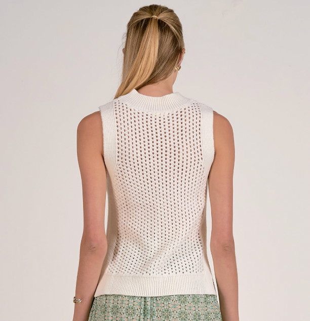 Woman wearing a white sleeveless knitted top against a plain background