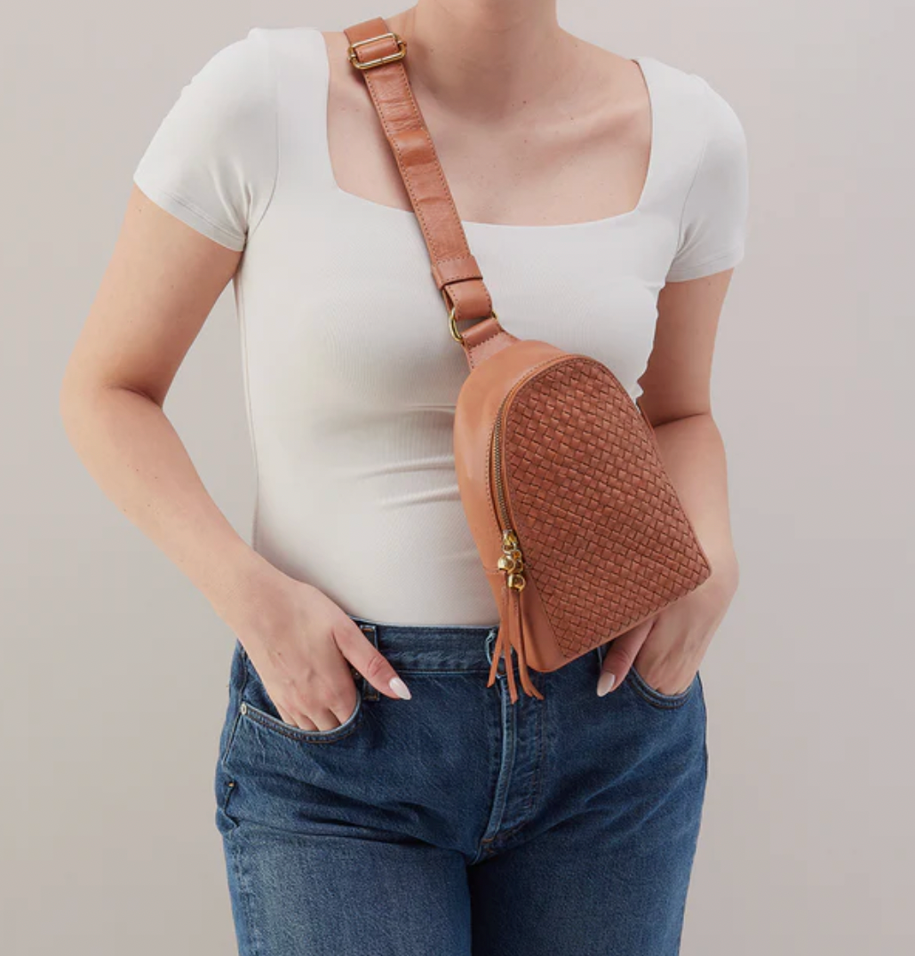 Person wearing a brown woven crossbody bag with a plain background