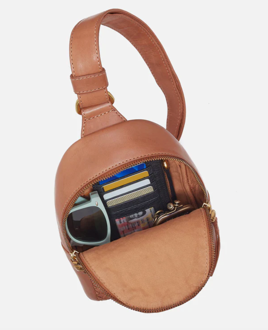 Brown leather crossbody bag with sunglasses and cards on a light gray background