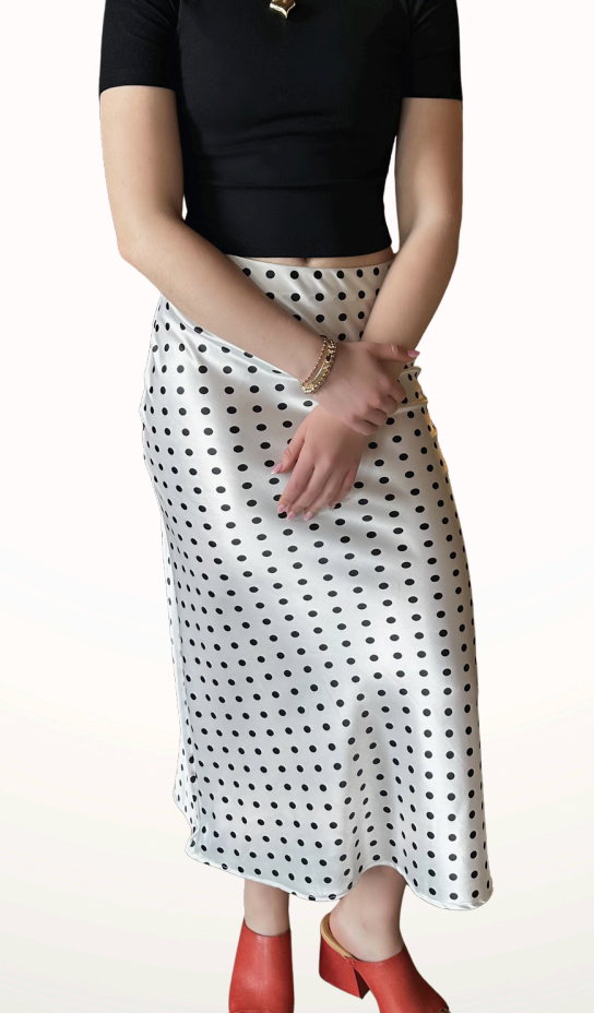 Person wearing a black top and white polka dot skirt on a plain background