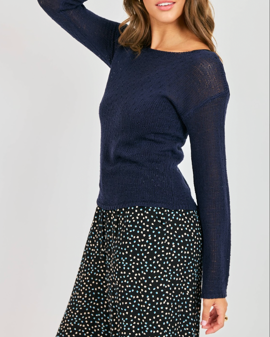 Woman wearing a navy sweater and polka dot skirt on a plain background