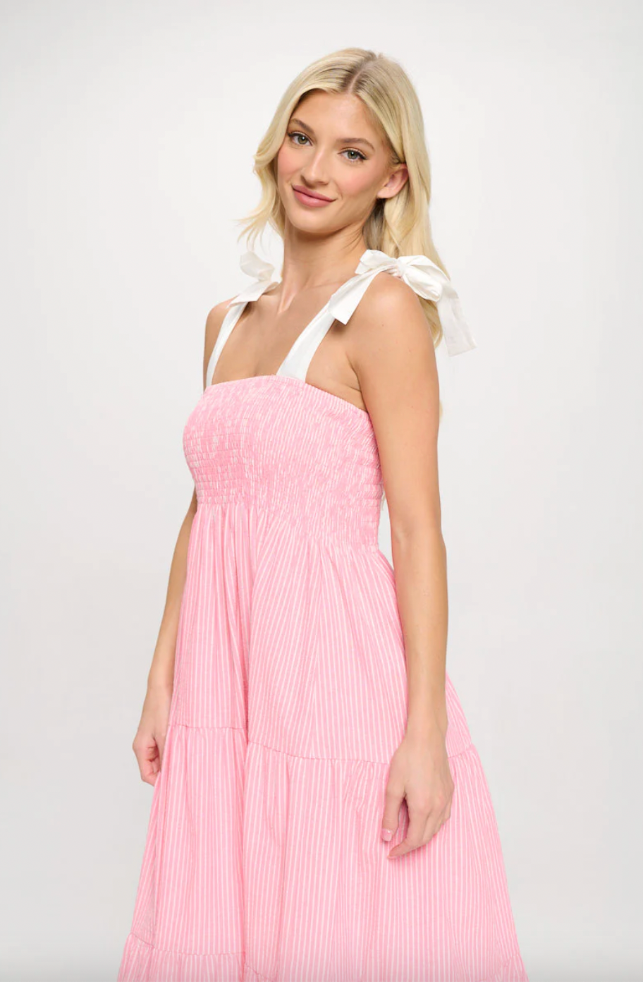 Woman wearing a pink dress with white straps on a plain background