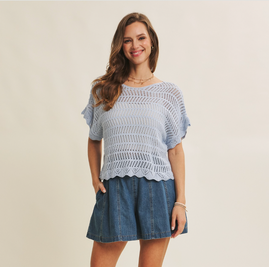 Woman wearing a light blue crochet top and denim skirt on a beige background