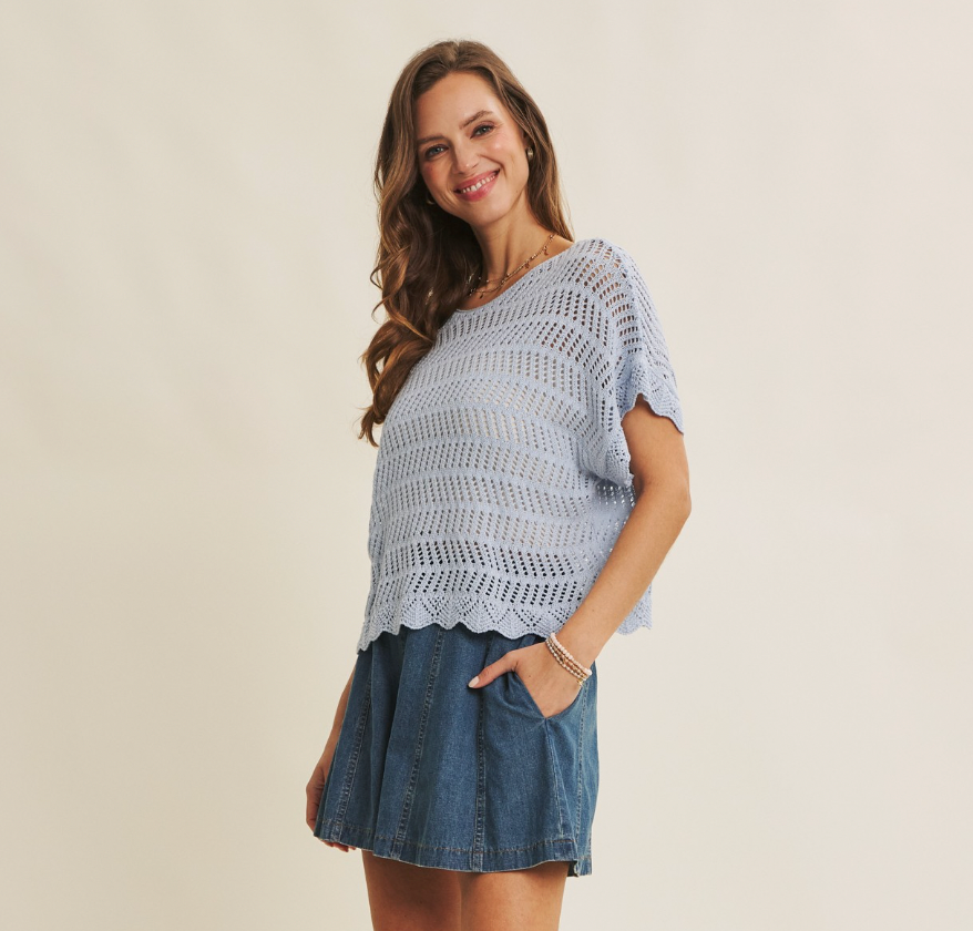 Woman wearing a light blue crochet top and denim skirt on a beige background