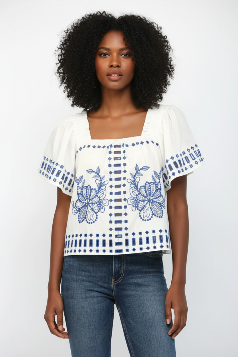 Woman wearing a white blouse with blue floral embroidery and blue jeans on a white background