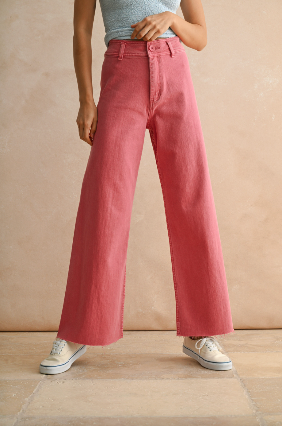 Person wearing pink wide-leg jeans and white sneakers on a beige background