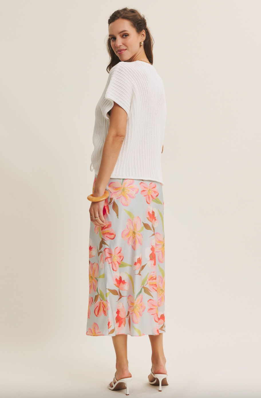 Woman wearing a white top and floral skirt on a plain background