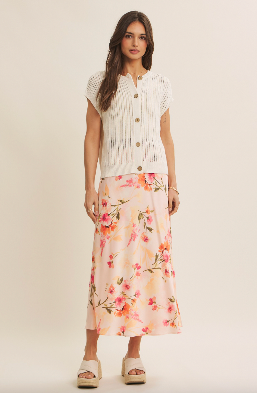 Woman wearing a white cardigan and floral skirt on a plain background