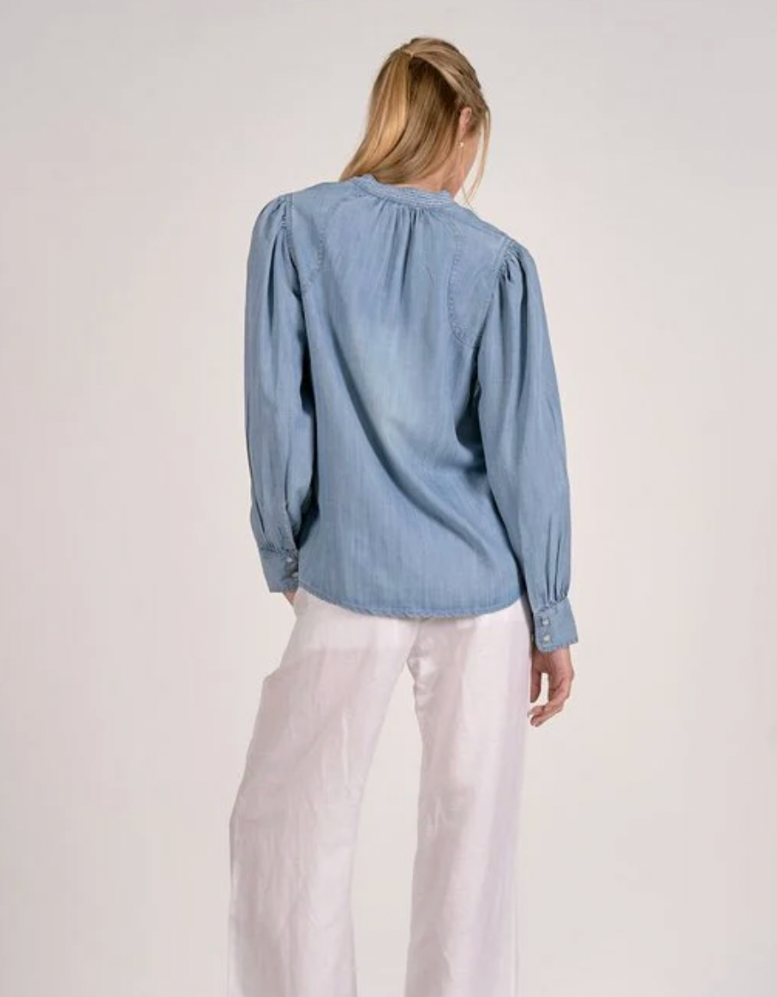 Person wearing a blue denim shirt and white pants on a plain background