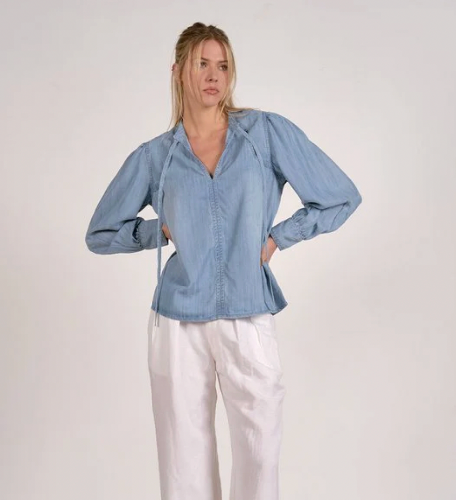 Woman wearing a blue denim shirt and white pants against a plain background