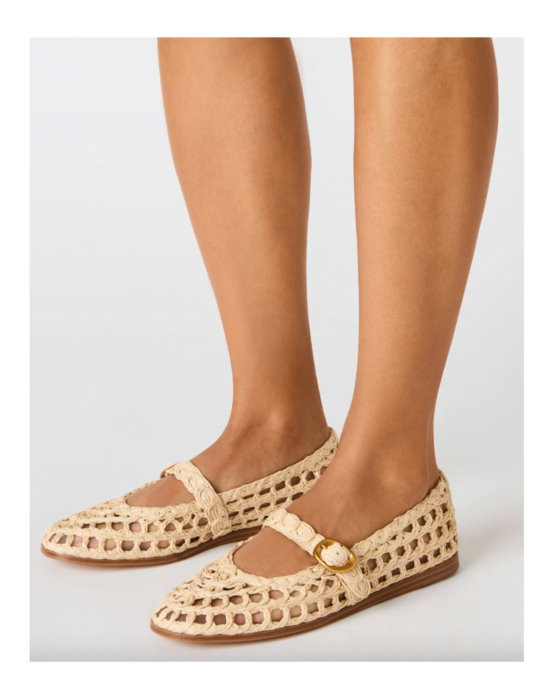 Beige woven shoes with a gold buckle worn by a person on a light gray background