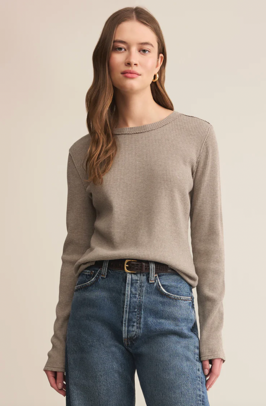 Woman wearing a beige sweater and blue jeans against a plain background