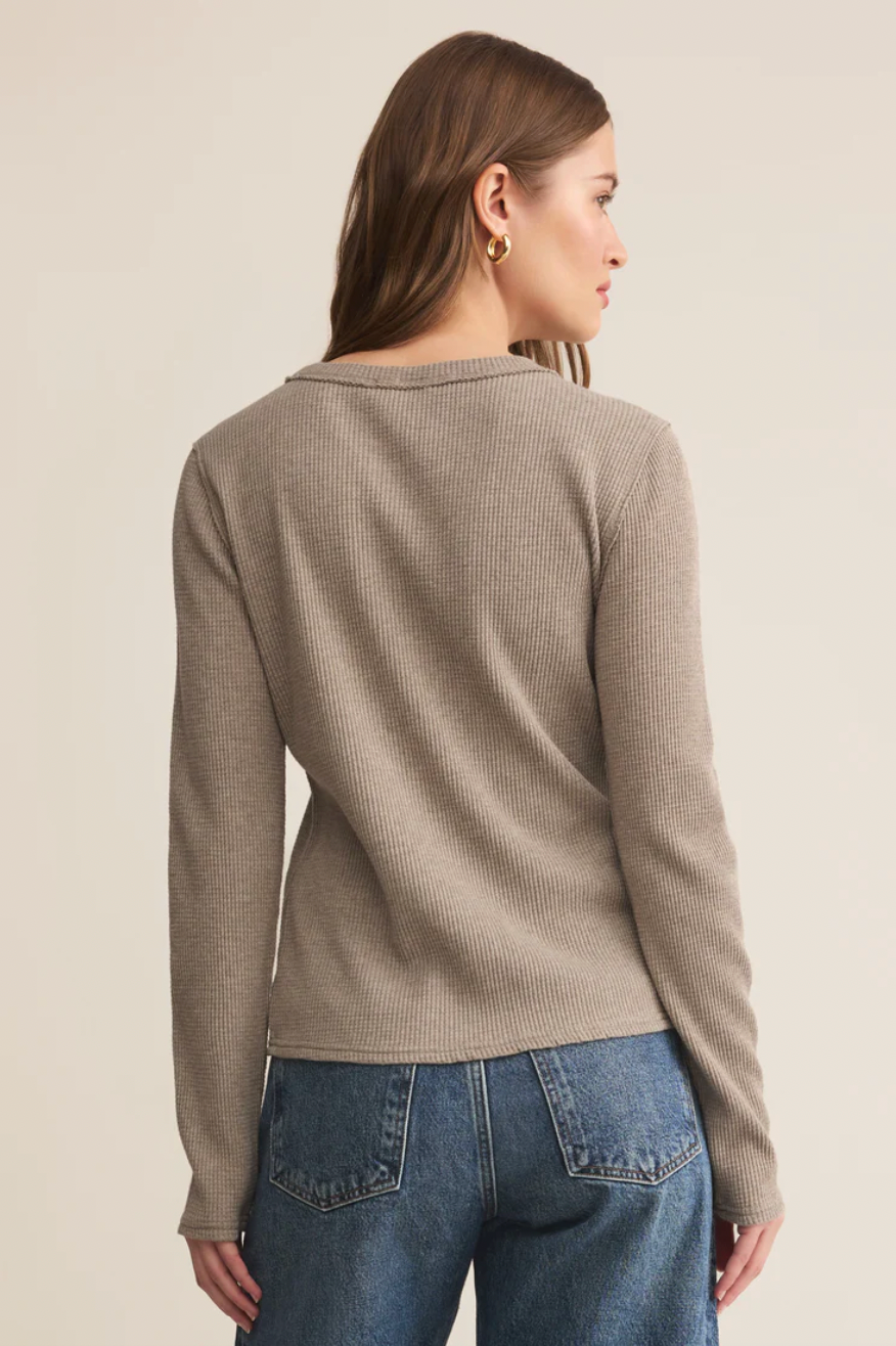 Woman wearing a beige long-sleeve shirt and blue jeans on a beige background