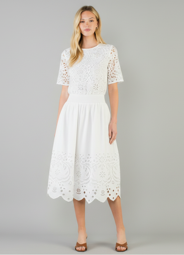 Woman wearing a white dress with lace details on a plain background