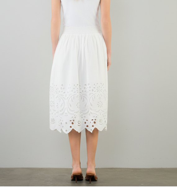 Woman wearing a white dress with lace details on a plain background