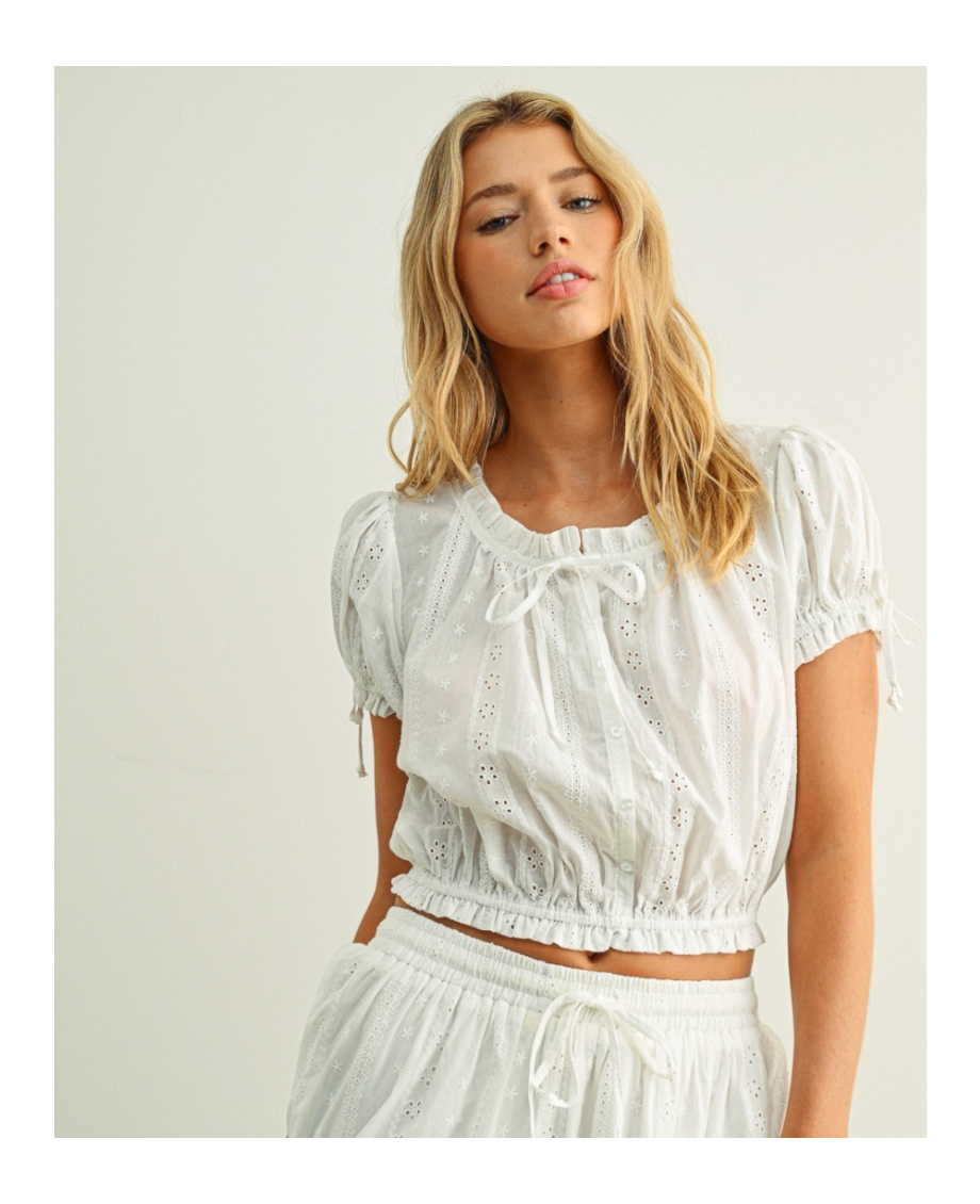 Woman wearing a white embroidered top and skirt against a plain background