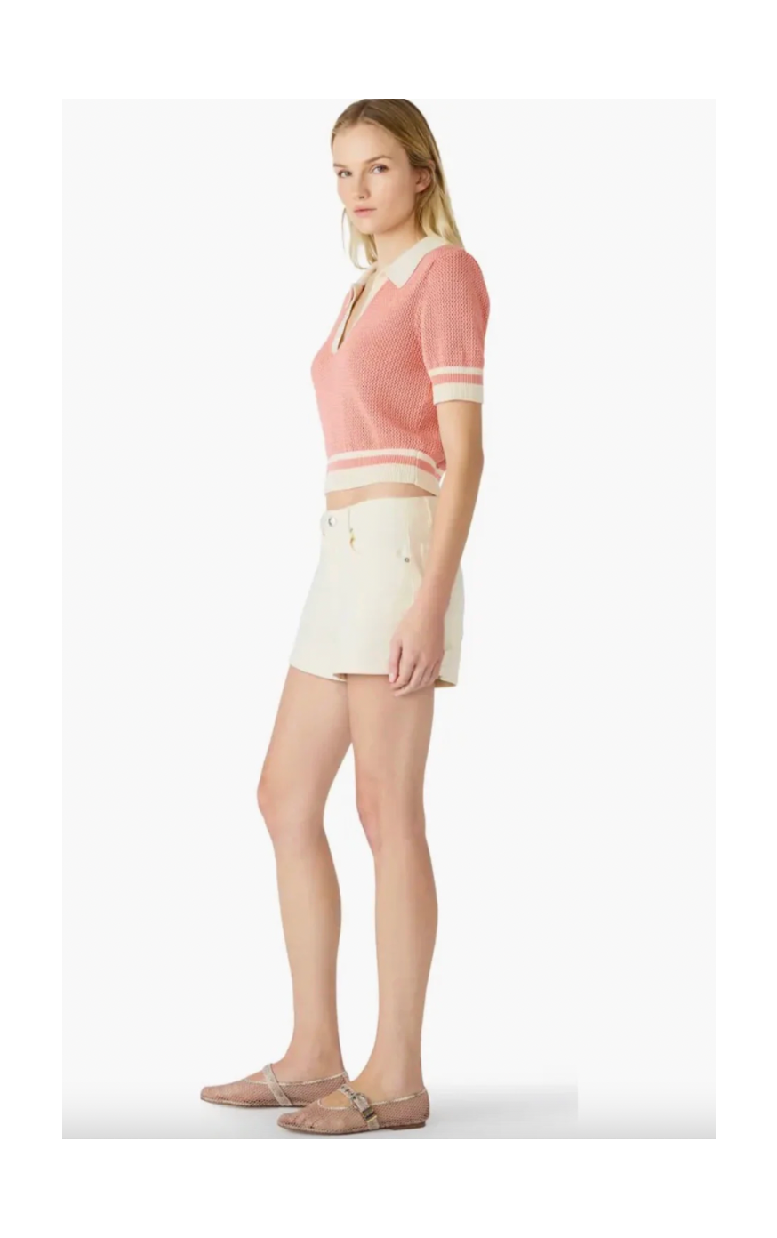 Woman wearing a pink knit top and white shorts on a white background