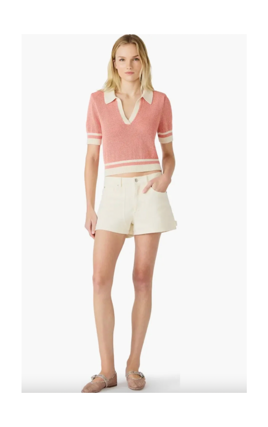 Woman wearing a pink and white striped polo shirt with a collar and cream shorts on a white background