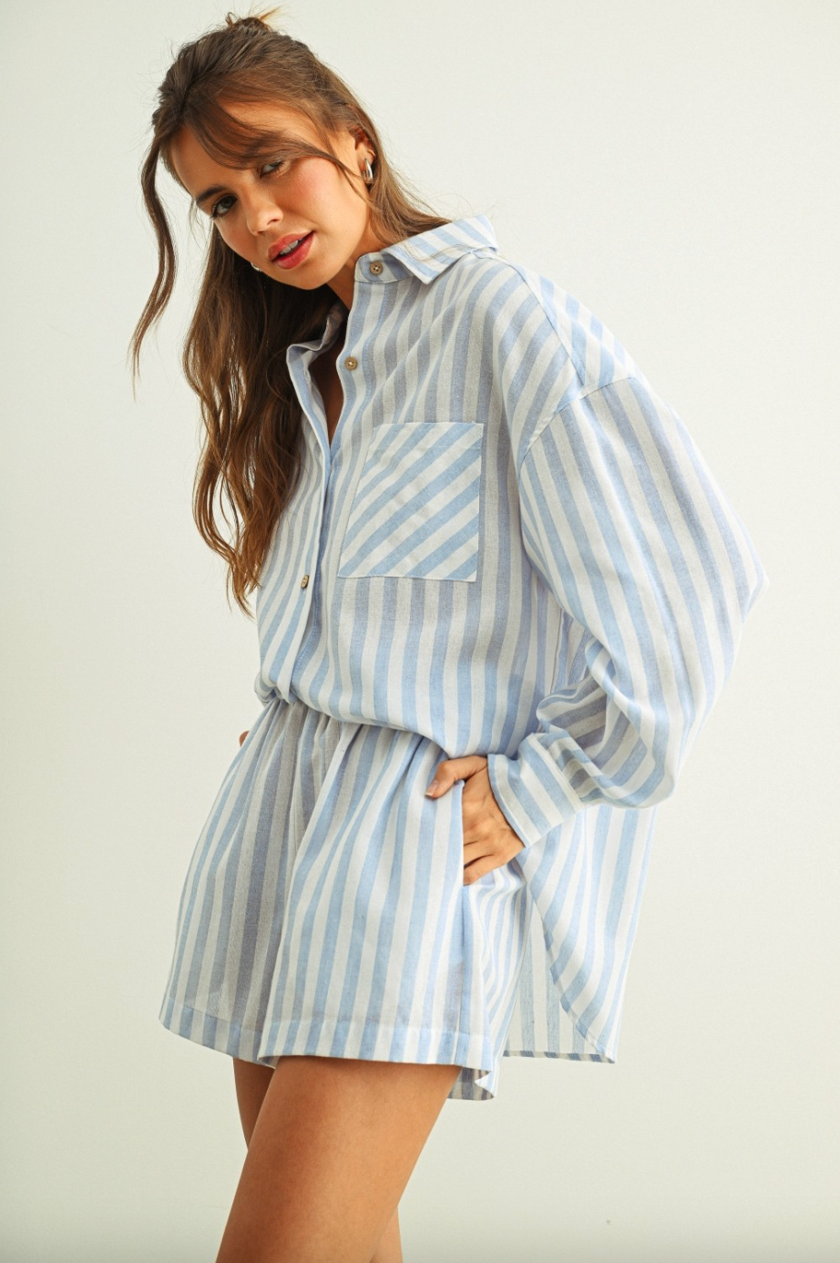 Woman wearing a light blue and white striped shirt and shorts set on a plain background