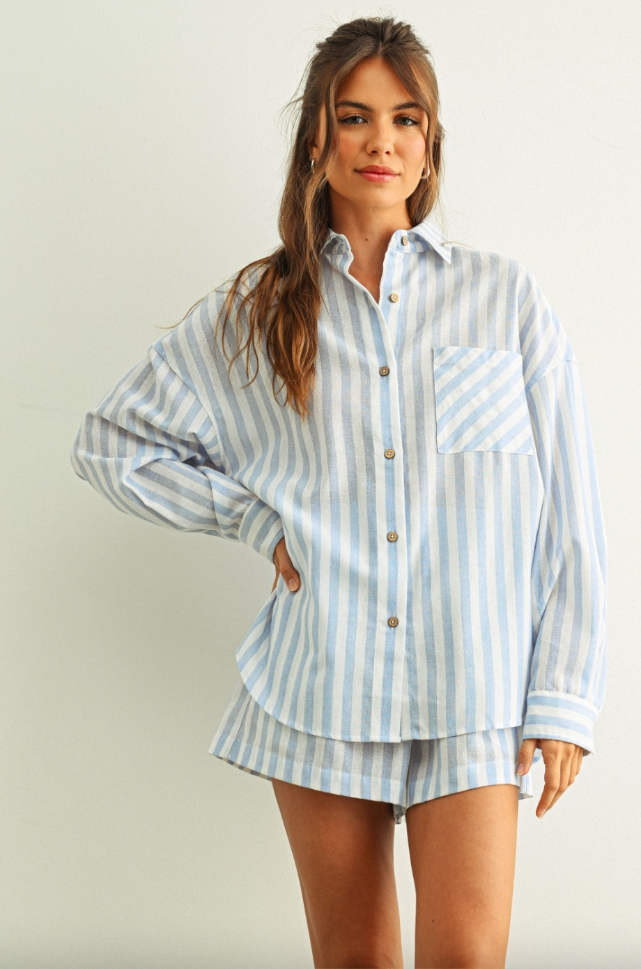 Woman wearing a light blue and white striped pajama set against a plain background