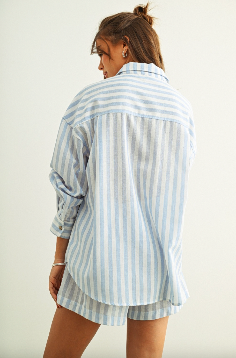 Woman wearing a light blue and white striped shirt and shorts on a plain background